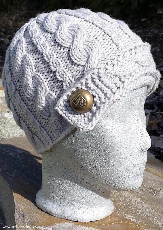 Hellgraue gestrickte Mütze mit Zopfmuster und bronzefarbenem Zierknopf auf Mannequinkopf, Seitenansicht.