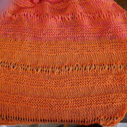 Nahaufnahme gestrickter Fläche in Orange und Pink mit offenen Reihen (Drop‑Stitch) und Verlaufsgarn