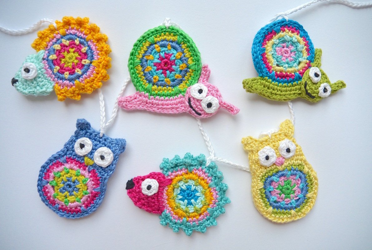 Sechs bunte gehäkelte Tier-Applikationen (Igel, Schnecken, Eulen) an weißer Schnur.