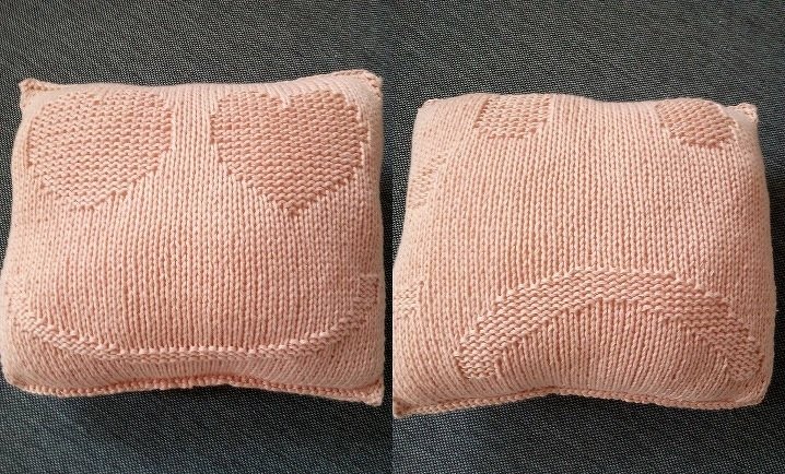 Zwei rosafarbene gestrickte Kissen auf dunklem Stoff, links mit Herzaugen und Lächeln, rechts mit traurigem Gesicht