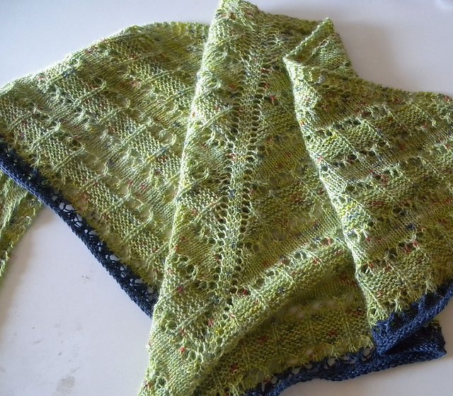 Light green knitted lace shawl with a dark blue border, folded on a white surface