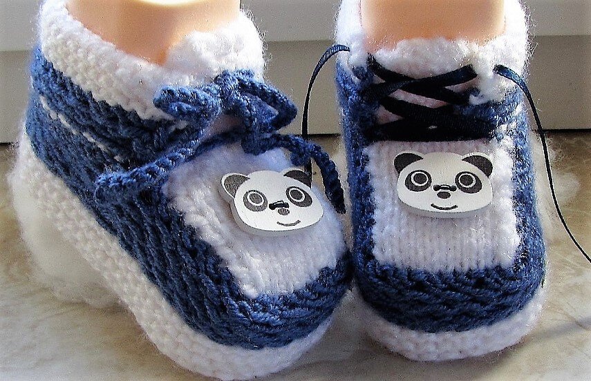 Paar gestrickter blau-weißer Babyschuhe mit Panda-Applikation und Schnürung