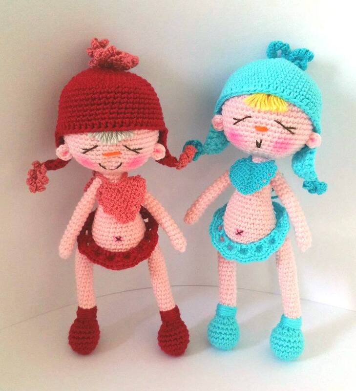 Zwei handgehäkelte Amigurumi-Püppchen in Rot und Türkis mit Mützen und Röcken.