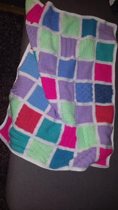 Gestrickte Babydecke mit verschiedenen Quadratmustern und weißer Einfassung