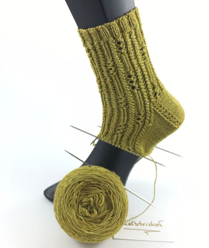 Handgestrickte olivgrüne Damensocke auf Fußmodell mit Garn und Stricknadeln