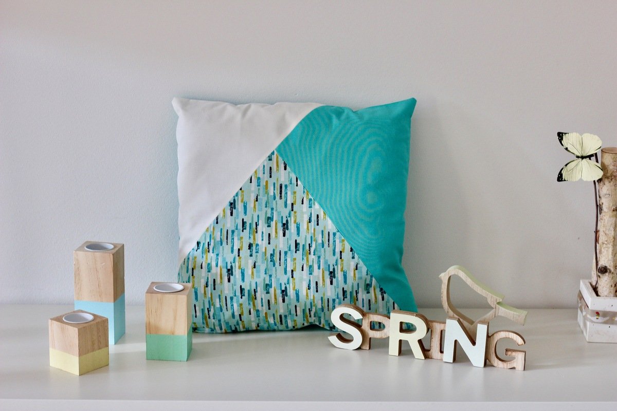 DIY-Kissenbezug mit Dreiecksblock in Türkis, Weiß und gemustertem Stoff auf Sideboard mit pastellfarbenen Holzkerzenhaltern