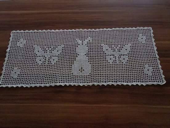 Weiß gehäkelter rechteckiger Tischläufer im Filet-Muster mit Hasen- und Schmetterlingsmotiven auf dunklem Holztisch