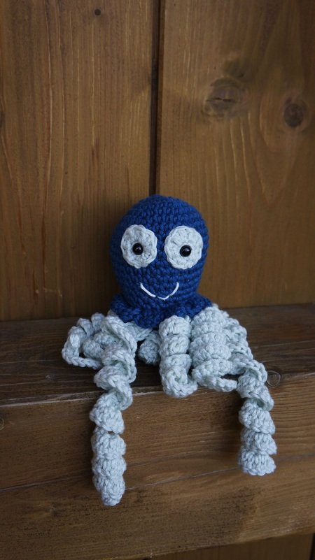 Gehäkelter blauer Oktopus mit hellgrauen spiralförmigen Tentakeln auf Holz