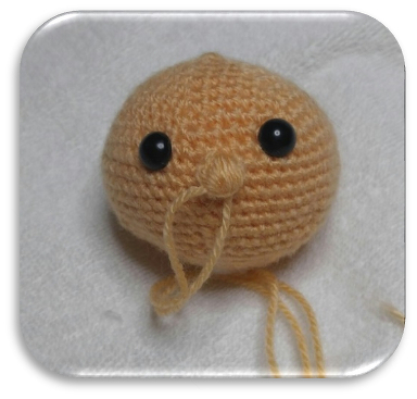 Beiger gehäkelter Amigurumi-Kopf mit schwarzen Sicherheitsaugen und Garnenden