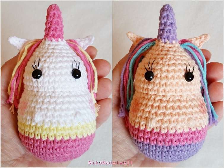Zwei kleine Amigurumi-Einhörner, eines weiß mit rosa Akzenten, das andere pfirsichfarben mit bunten Mähnen, in einer Hand gehalten.