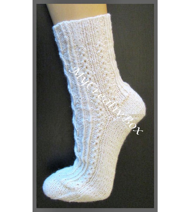 Wadenlange weiße gestrickte Socke mit Ajour- und Zopfmuster vor dunklem Hintergrund