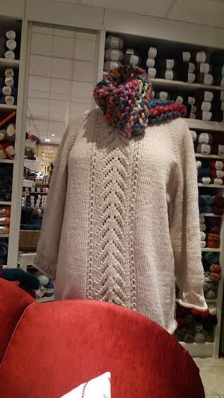 Mannequin trägt beigefarbenen Strickpullover mit Lochmuster und mehrfarbigem Loopschal