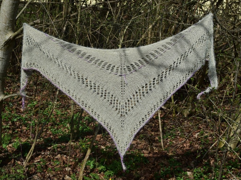 Gestricktes Dreieckstuch mit Ajourreihen und dezenter lila Randkante, aufgehängt an Zweigen