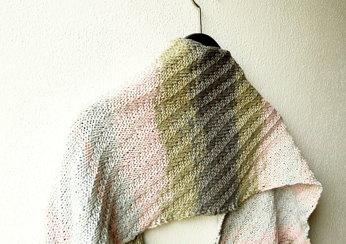 Gestricktes Rechtecktuch mit diagonaler Rippenstruktur und Farbverlauf, aufgehängt an einem Bügel