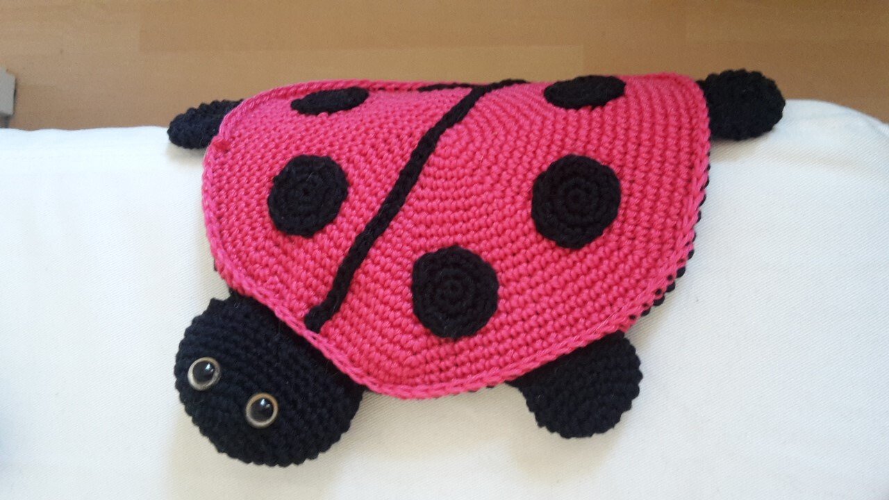 Gehäkeltes Marienkäfer-Schmusetuch in Pink mit schwarzen Punkten und schwarzem Kopf auf hellem Untergrund.