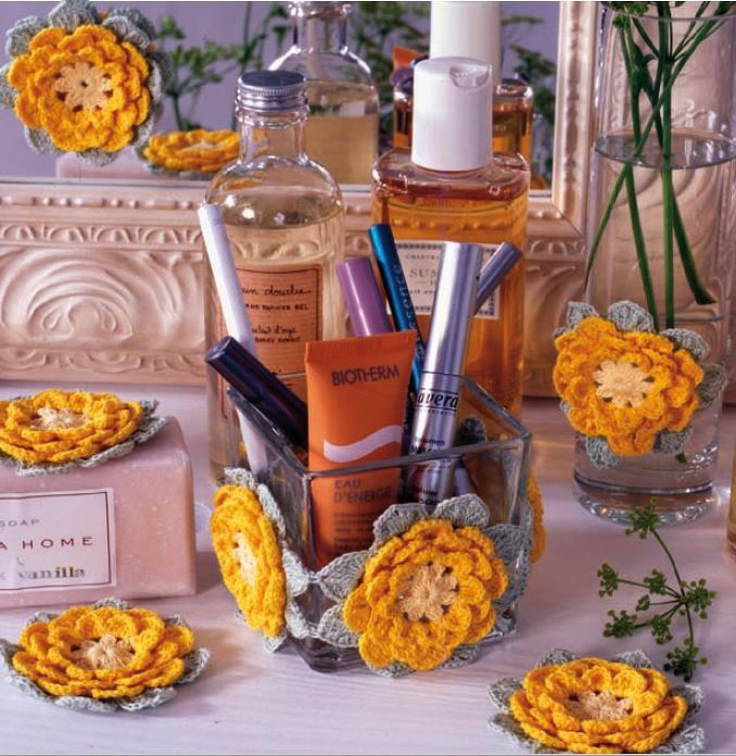 Gehäkelte gelbe Blüten als Untersetzer unter Kosmetikprodukten auf einem hellen Waschtisch
