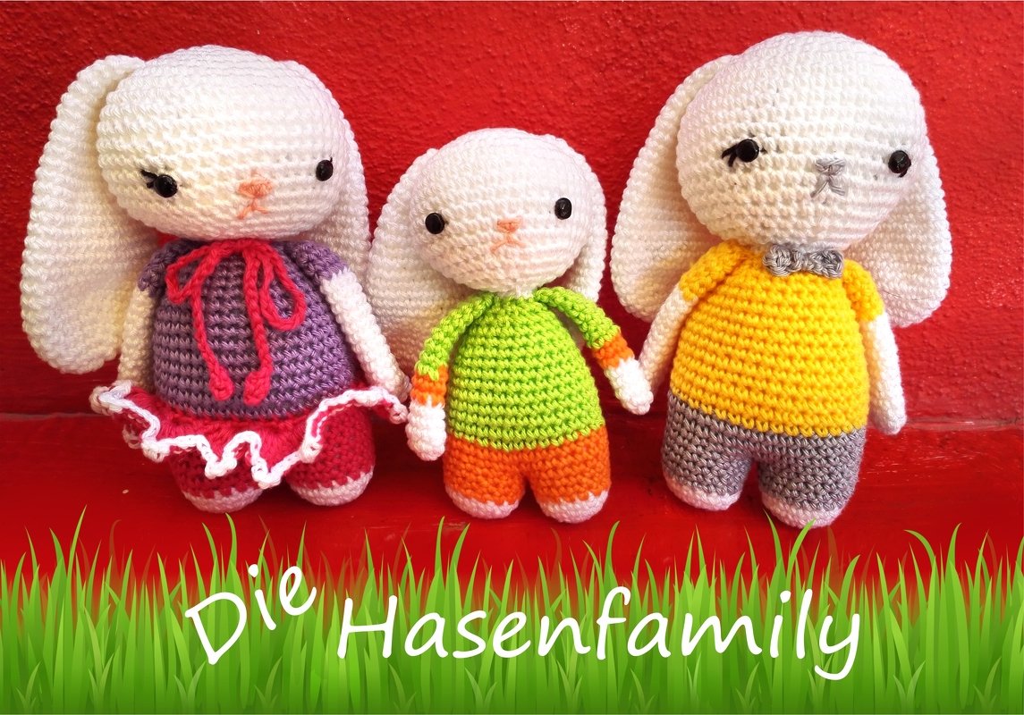 Drei handgehäkelte weiße Hasen in bunten Outfits vor rotem Hintergrund mit Grasdekor