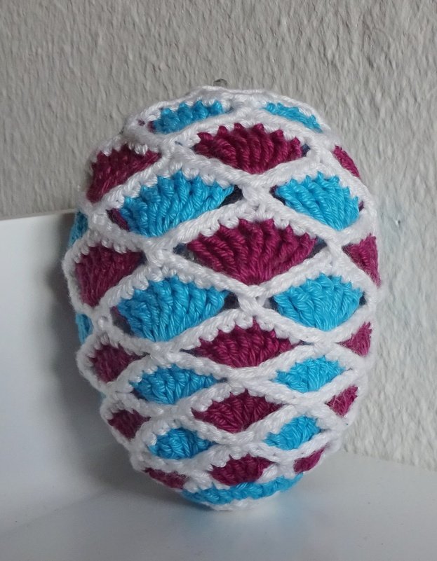 Gehäkeltes Osterei mit weißem Gitter und Einsätzen in Türkis und Magenta