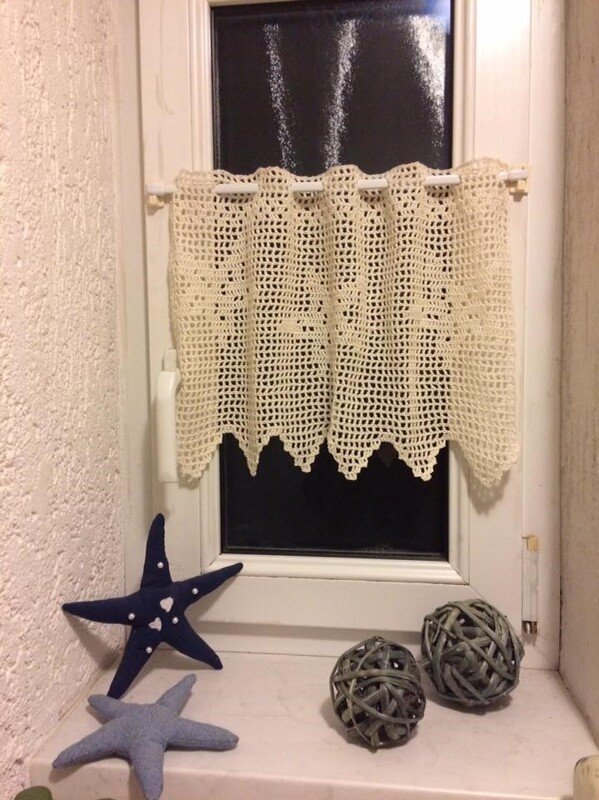 Handgehäkelter, cremefarbener Vorhang mit Muschelmuster an kleinem Fenster; Stoff-Seesterne und geflochtene Kugeln auf der Fensterbank.