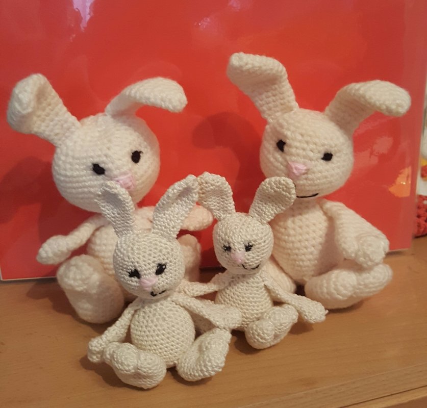 Vier gehäkelte Amigurumi-Hasen in Cremefarben, zwei große und zwei kleine, vor rotem Hintergrund