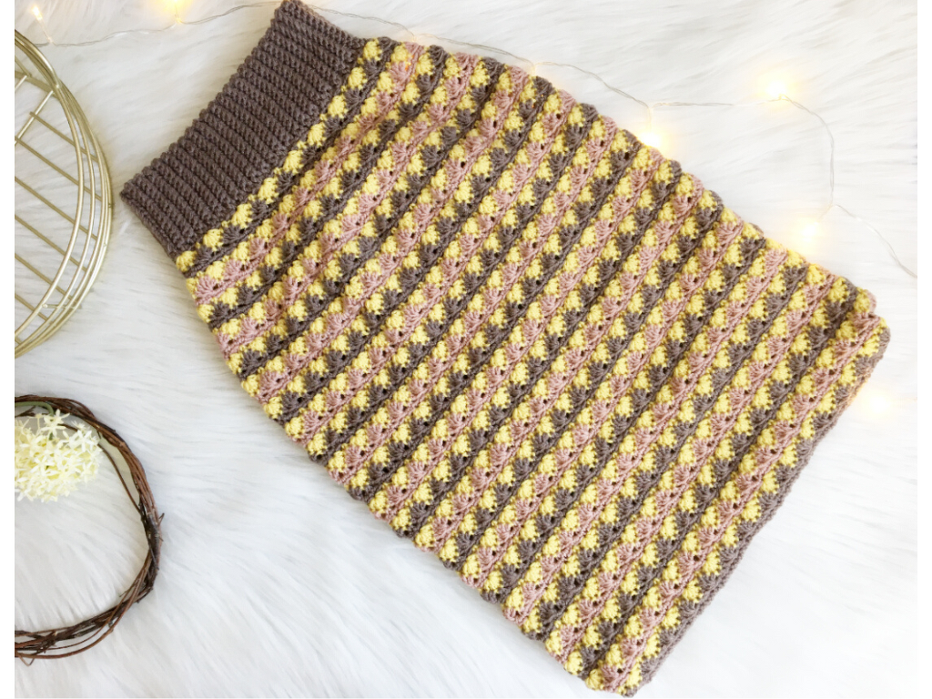 Flach gelegter gehäkelter Babysack mit elastischem Rippenbündchen und gelb-rosa Streifen auf braunem Grund