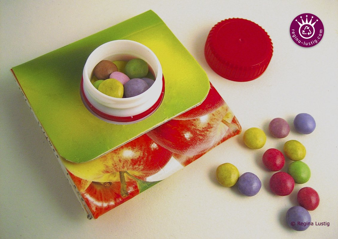 Grün-rote Papierverpackung mit Apfelmuster, geöffnete Dose bunter Süßigkeiten und verstreute Bonbons