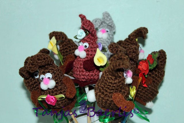 Gehäkelte Amigurumi-Hasen auf Holzstäben mit kleinen Blumen