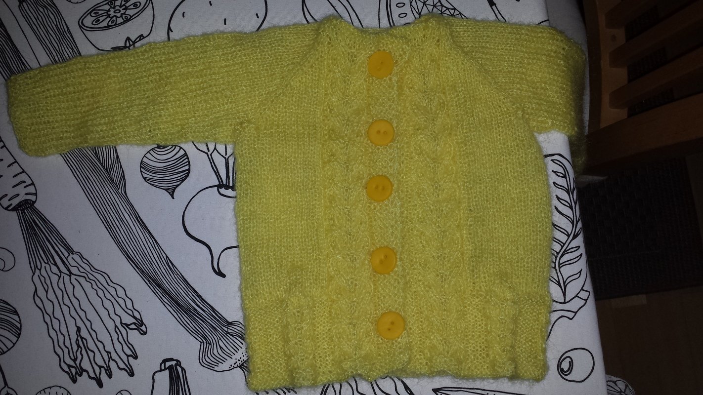 Gelbe gestrickte Babyjacke mit fünf Knöpfen auf gemustertem Untergrund
