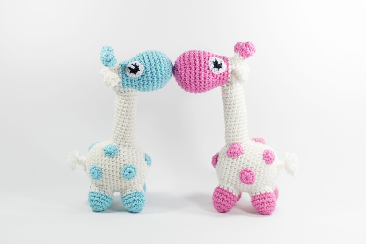 Zwei gehäkelte Amigurumi-Giraffen in Hellblau und Rosa mit den Köpfen aneinander
