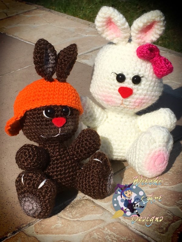 Zwei gehäkelte Amigurumi-Hasen (braun mit oranger Mütze, weiß mit pinker Schleife) auf Fliesen