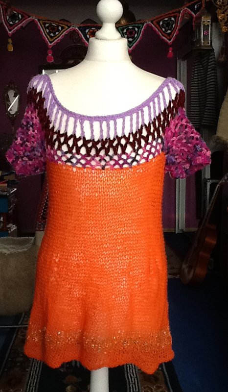 Gestricktes orangefarbenes Damen-Shirt mit mehrfarbigem Carmen-Ausschnitt auf einer Schneiderpuppe.