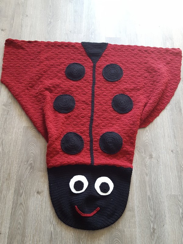 Gehäkelte rote Marienkäfer-Decke mit schwarzen Punkten und Kapuze mit Augen und Mund