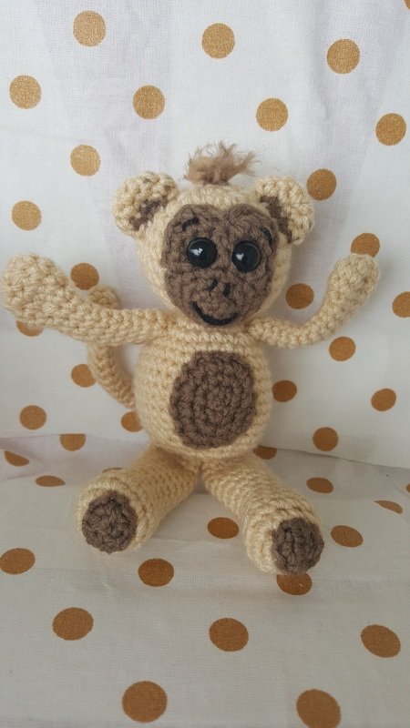 Gehäkelter Amigurumi-Affe in Beige und Braun, sitzend vor weißem Hintergrund mit goldenen Punkten