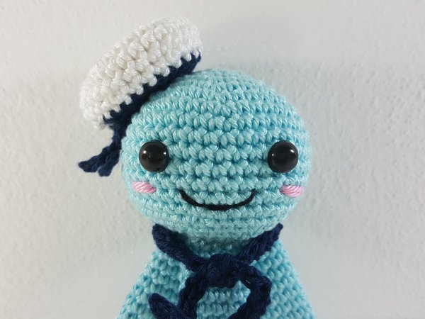 Hellblaue gehäkelte Amigurumi-Matrosenfigur mit weißer Mütze und blauem Halstuch