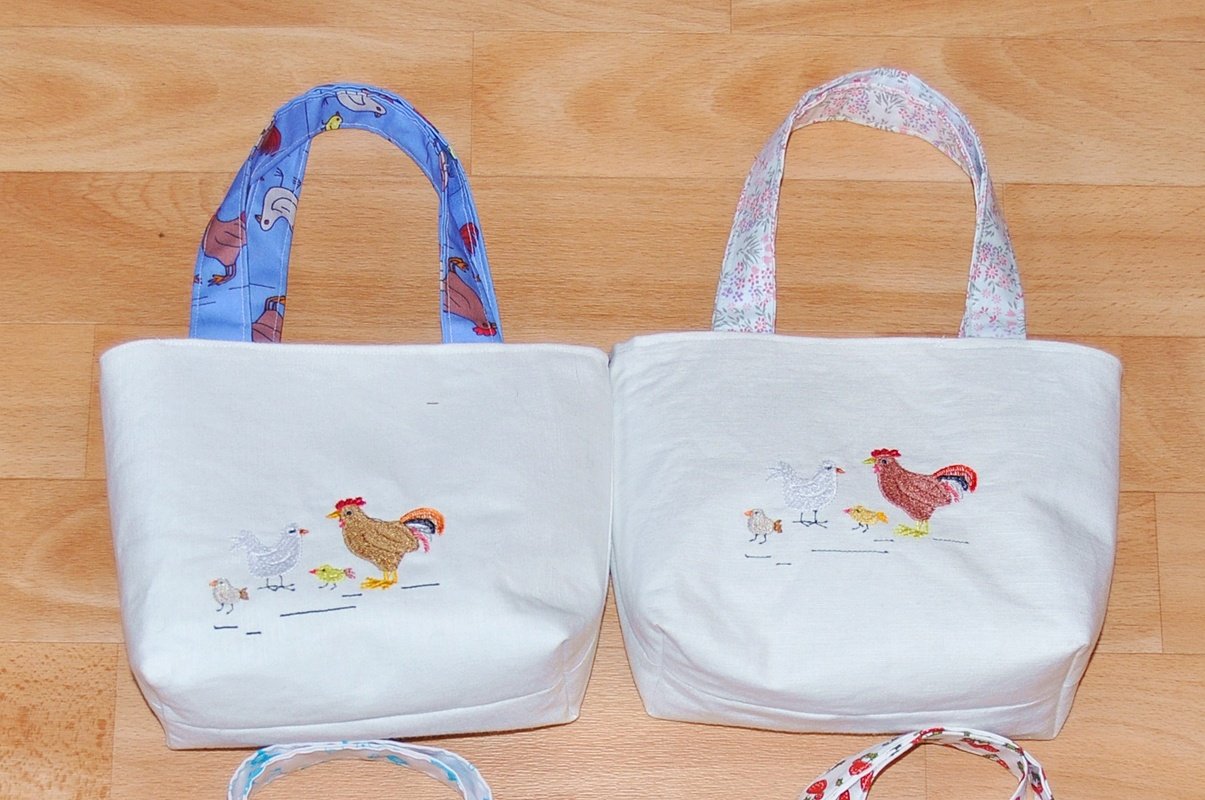 Zwei weiße Stofftaschen mit Hühner-Stickerei (Hahn, Henne, Küken).