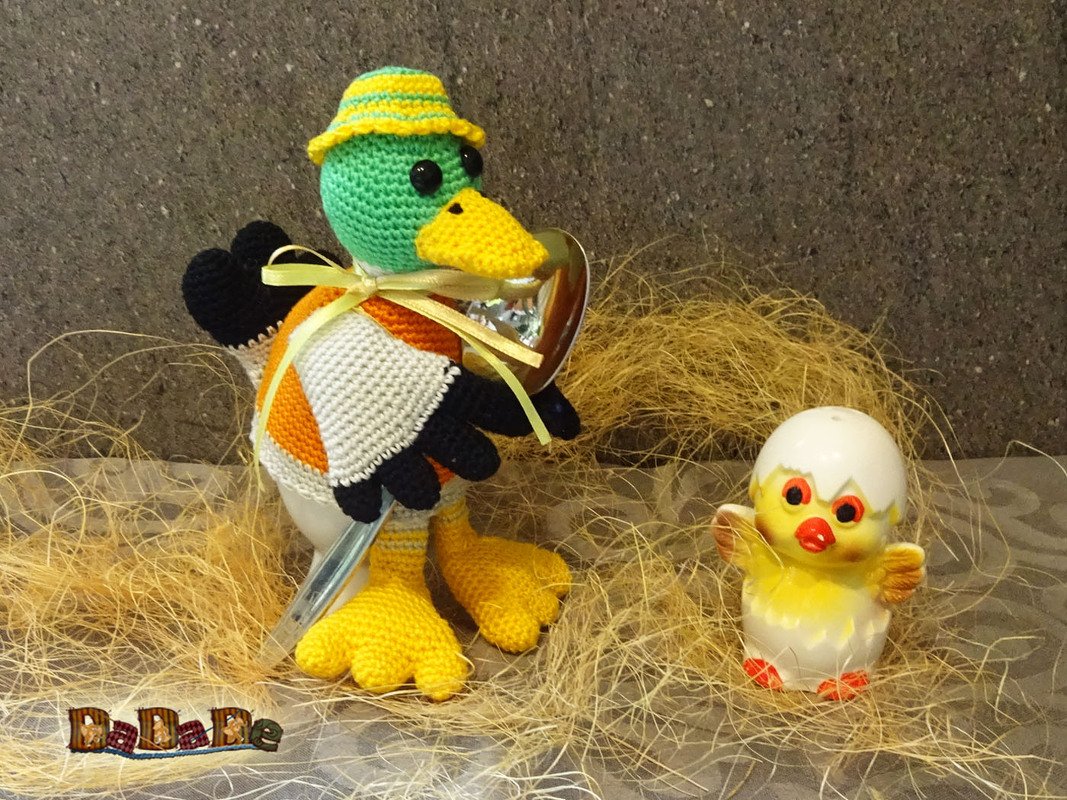 Gehäkelte Ente mit gestreiftem Hut und kleinem Küken auf Stroh