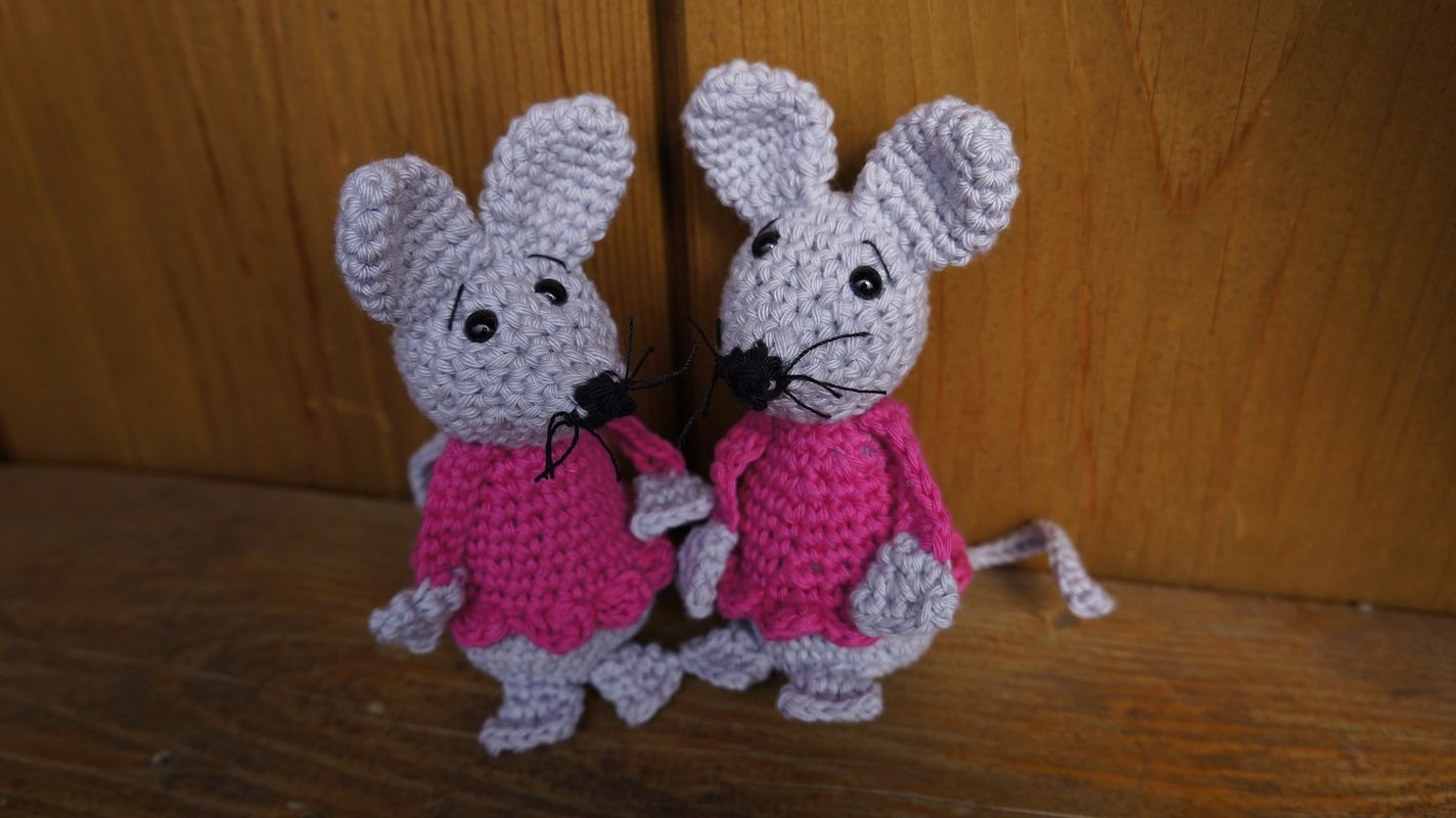 Zwei kompakte Amigurumi-Mäuse, gehäkelt in Grau mit pinken Kleidern