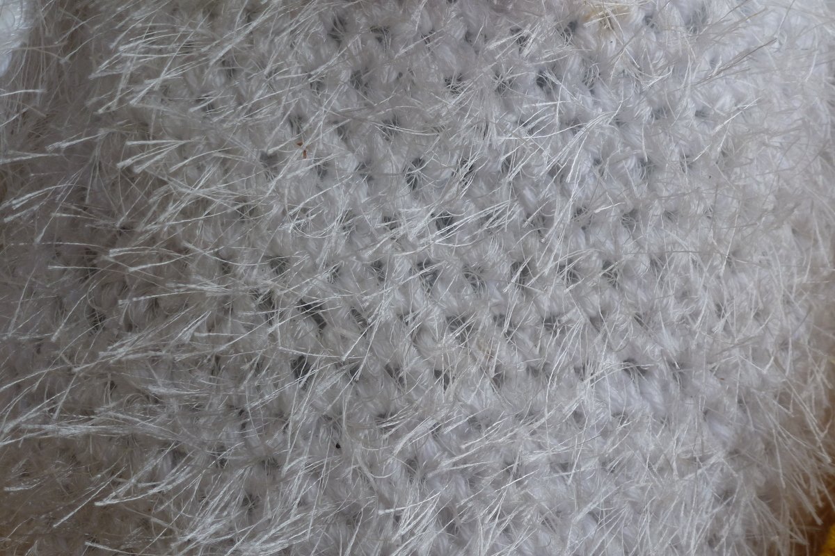 Nahaufnahme einer flauschigen weißen Häkeltextur mit langen, zarten Fasern und erkennbaren Maschen.
