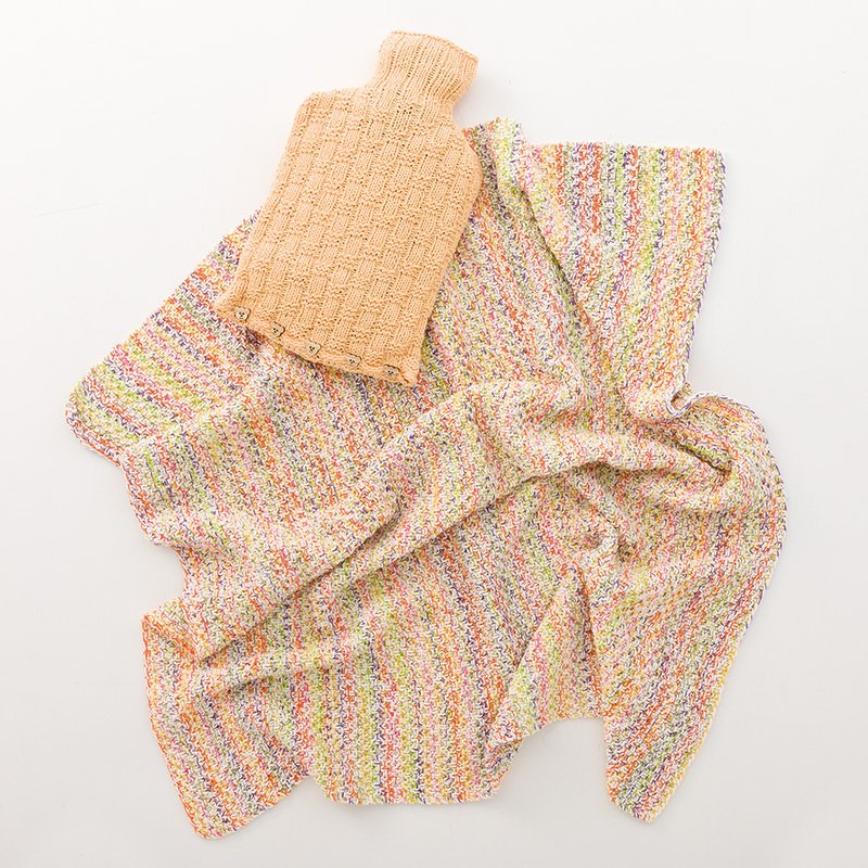 Gestrickte pfirsichfarbene Wärmflaschenhülle mit Knöpfen auf bunt melierter Strickdecke