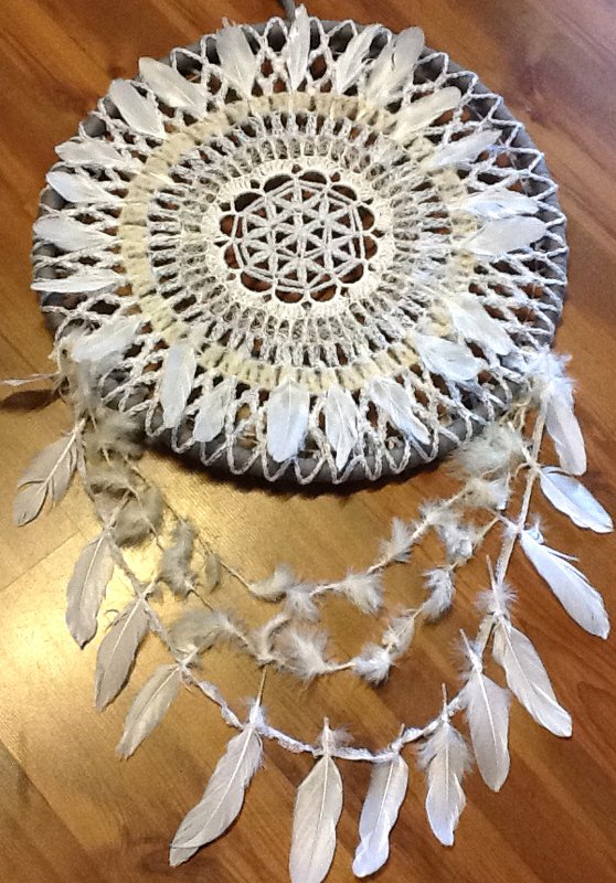 Runder gehäkelter Traumfänger aus weißem Garn mit Mandala-Muster und hängenden Federn auf Holzuntergrund
