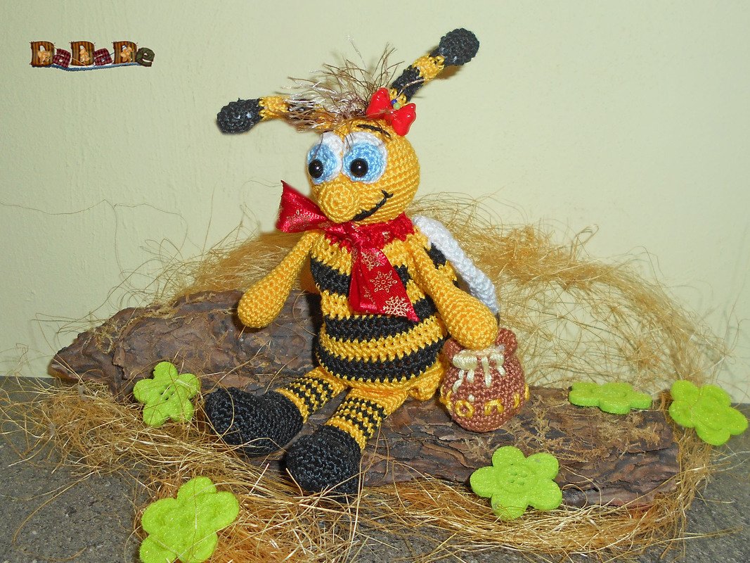 Gehäkelte gelb-schwarze Amigurumi-Biene mit roter Schleife und kleinem Honigtopf