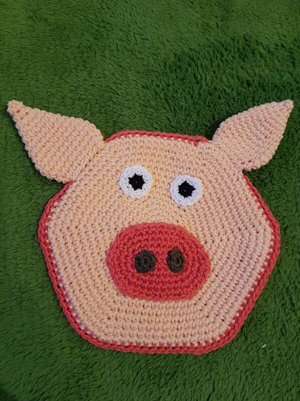 Handgehäkeltes Schweinchen‑Schmusetuch in Rosa und Koralle auf grünem Hintergrund