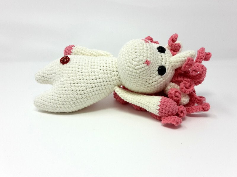 Gehäkeltes weißes Einhorn-Amigurumi mit rosa Lockenmähne, schwarzen Augen und Knopf, seitlich liegend