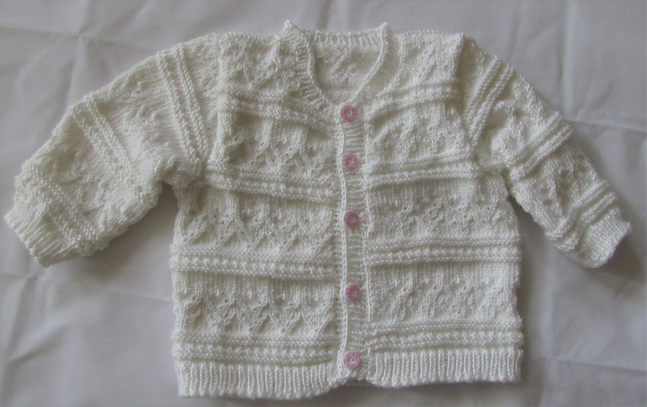 Weiße gestrickte Babyjacke mit Rundhalsausschnitt und fünf rosa Knöpfen