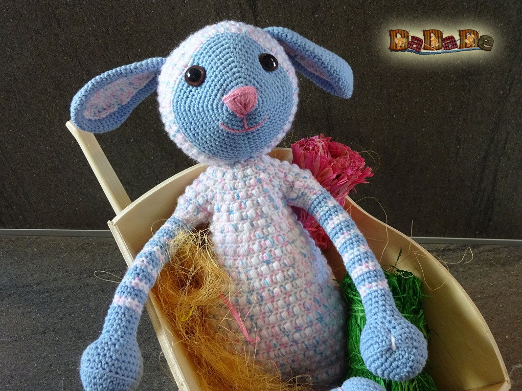 Gehäkeltes Schäfchen in Hellblau und Weiß mit rosa Nase, sitzend in einer kleinen Holzschale.