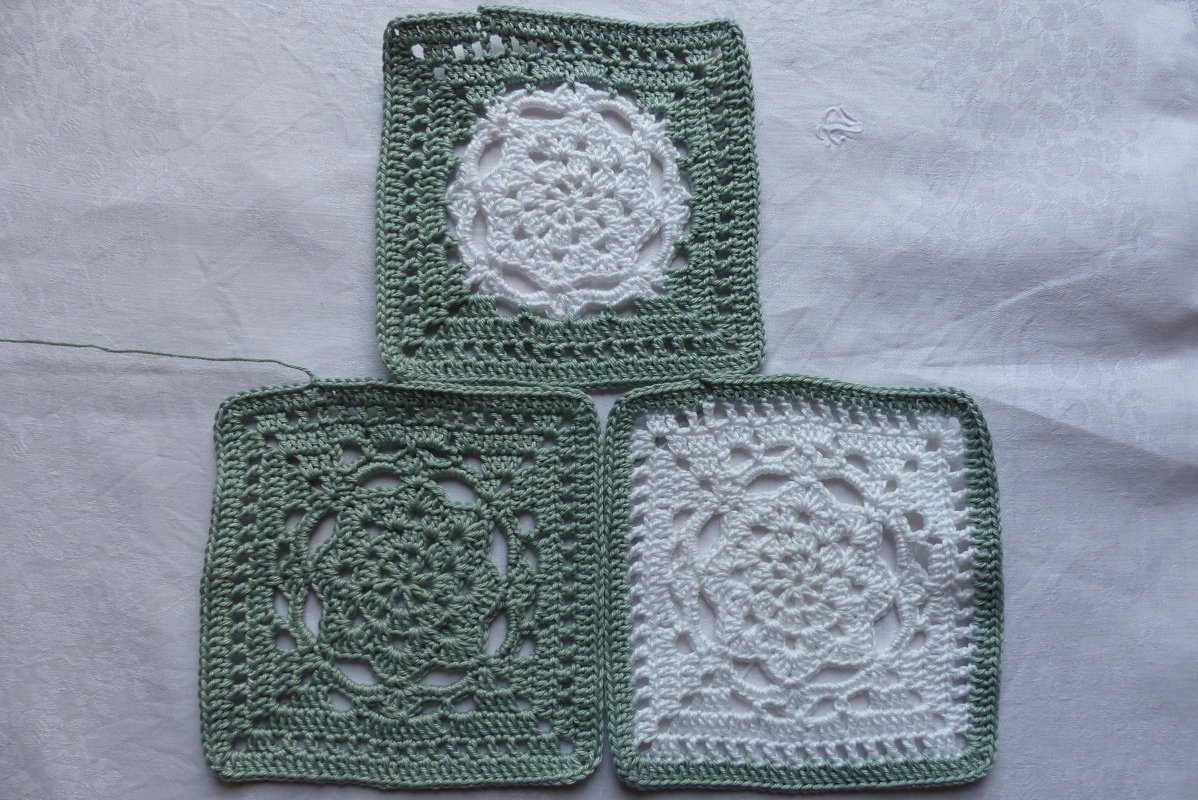Drei gehäkelte Granny Squares in Grün und Weiß auf hellem Stoff