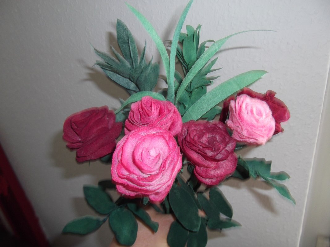 Strauß aus handgefertigten Rosen aus Stoff oder Papier in Rosa und Burgunderrot mit grünen Blättern.