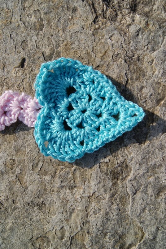 Türkises gehäkeltes Herz-Lesezeichen auf grauem, strukturiertem Stein mit rosa Kordel.