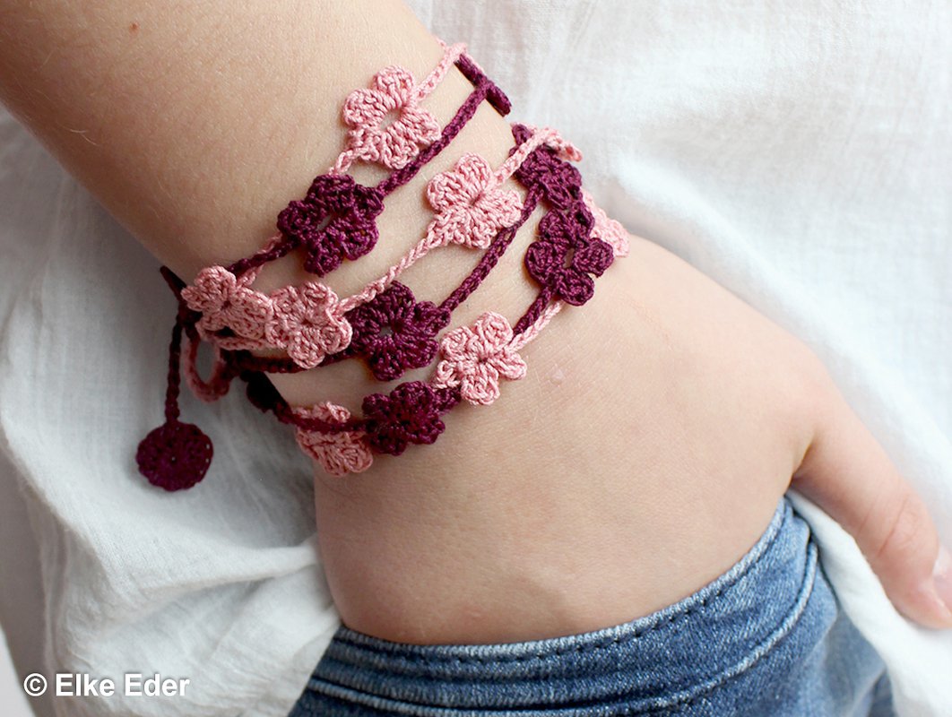 Gehäkeltes Armband mit kleinen rosa und bordeauxfarbenen Blüten am Handgelenk