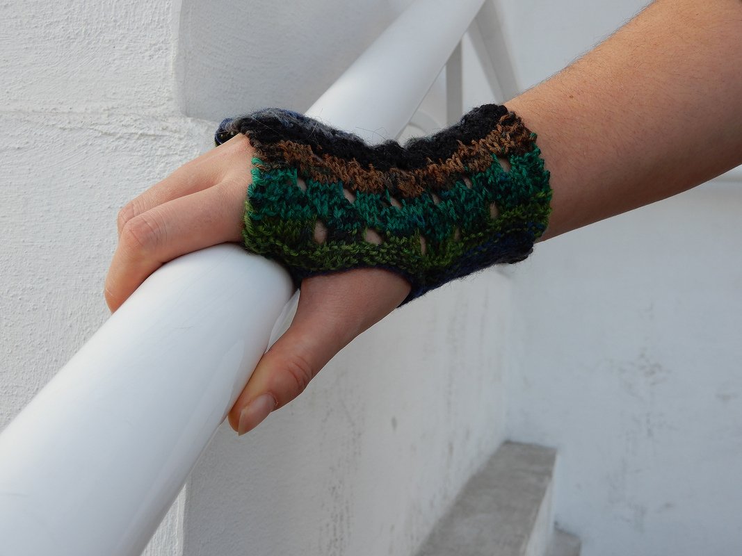 Hand trägt mehrfarbige gestrickte, fingerlose Armstulpe mit Daumenloch